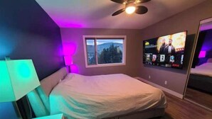 Une chambre à coucher avec un lit, un téléviseur fixé au mur, une fenêtre et un ventilateur de plafond.