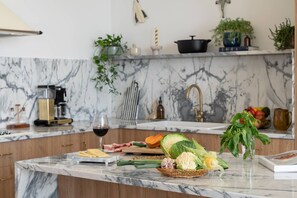 A marble kitchen counter with fresh vegetables, a wine glass, and various kitchen items.