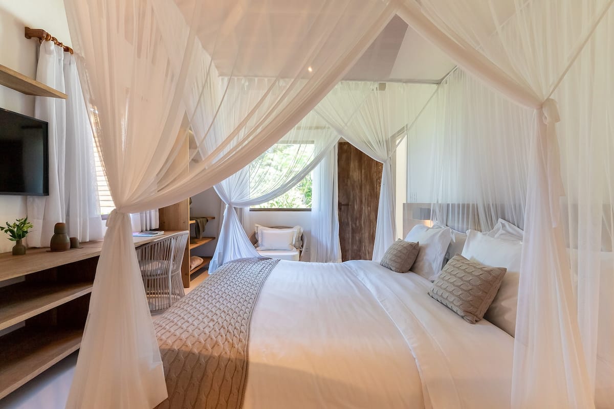 Ein Schlafzimmer mit Himmelsbett, Nachttisch, Fernseher und Blick ins Freie.