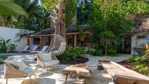 A tropical outdoor lounge area with wicker chairs, a hanging chair, and a wooden table.