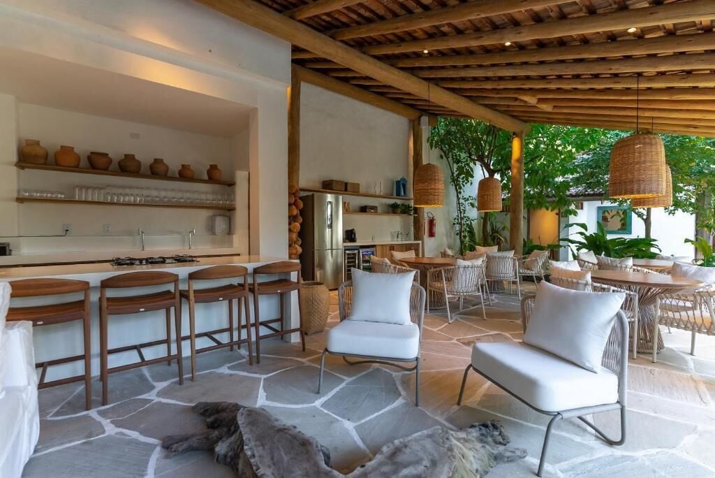 A modern kitchen with bar stools, a stone floor, and a dining area with wicker furniture.