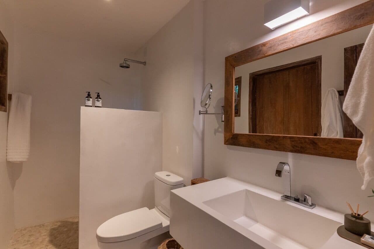 Un bagno moderno con lavandino bianco, mobile contenitore in legno, specchio e cabina doccia.