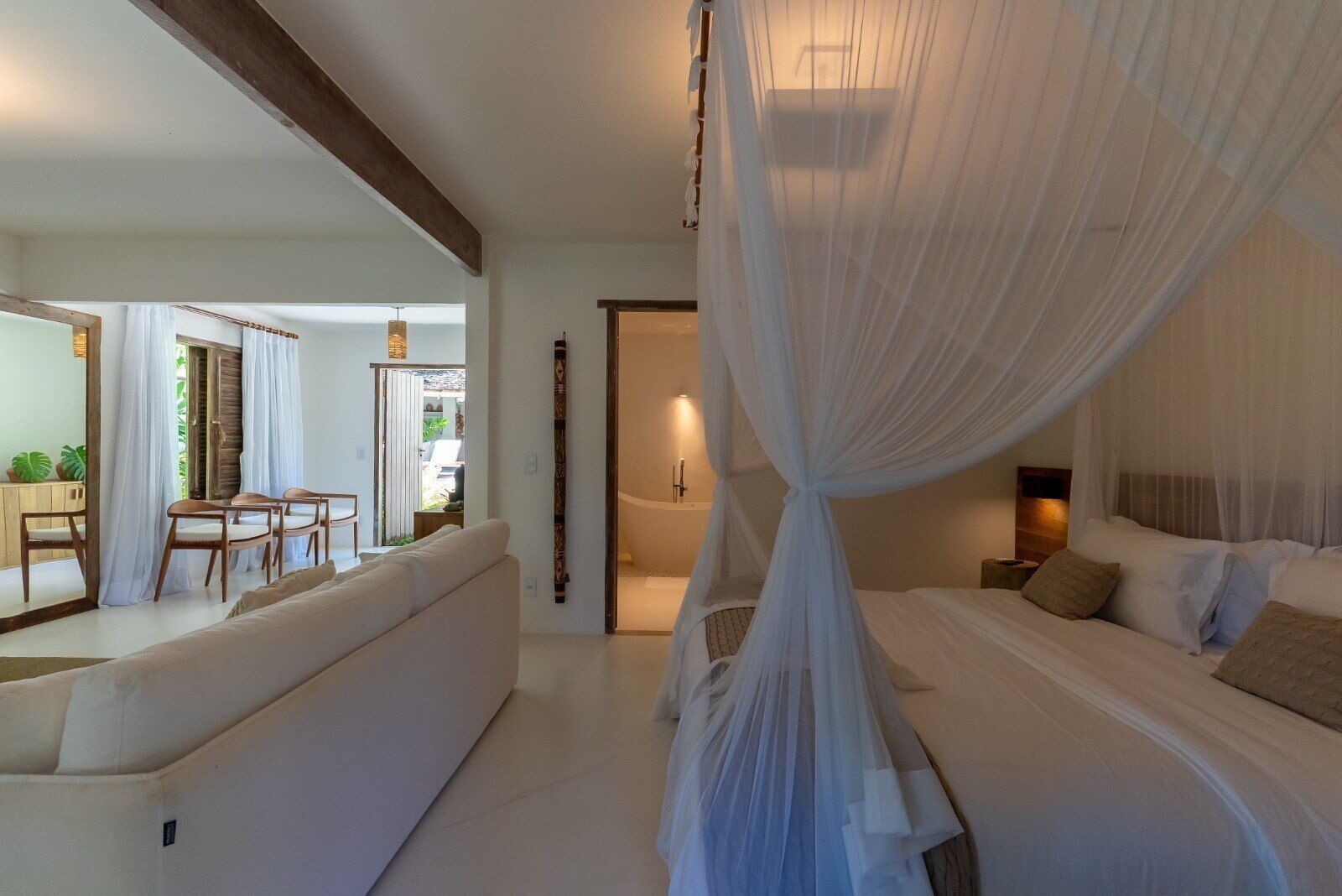 Un dormitorio con cama con dosel, una zona de estar con sofá y sillones, y vistas al exterior.