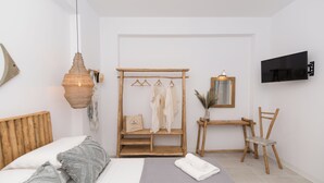 A modern bedroom with a wooden bed, a hanging light fixture, a wooden wardrobe, a desk with a chair, and a TV mounted on the wall.
