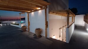 An outdoor patio area with a pergola, two large planters, and a view of the sunset.