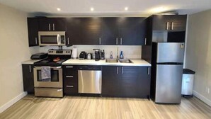 A modern kitchen with dark cabinetry, stainless steel appliances, and a light-colored countertop. - Private 1bd 1 ba suite w/ lake views (Vernon)