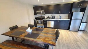 A modern kitchen with dark cabinetry, stainless steel appliances, and a wooden dining table with benches. - Private 1bd 1 ba suite w/ lake views (Vernon)