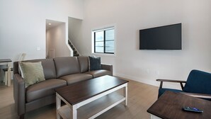 Ein modernes Wohnzimmer mit einem braunen Ledersofa, einem Holztisch und einem blauen Sessel. Ein Flachbildfernseher ist an der Wand befestigt.