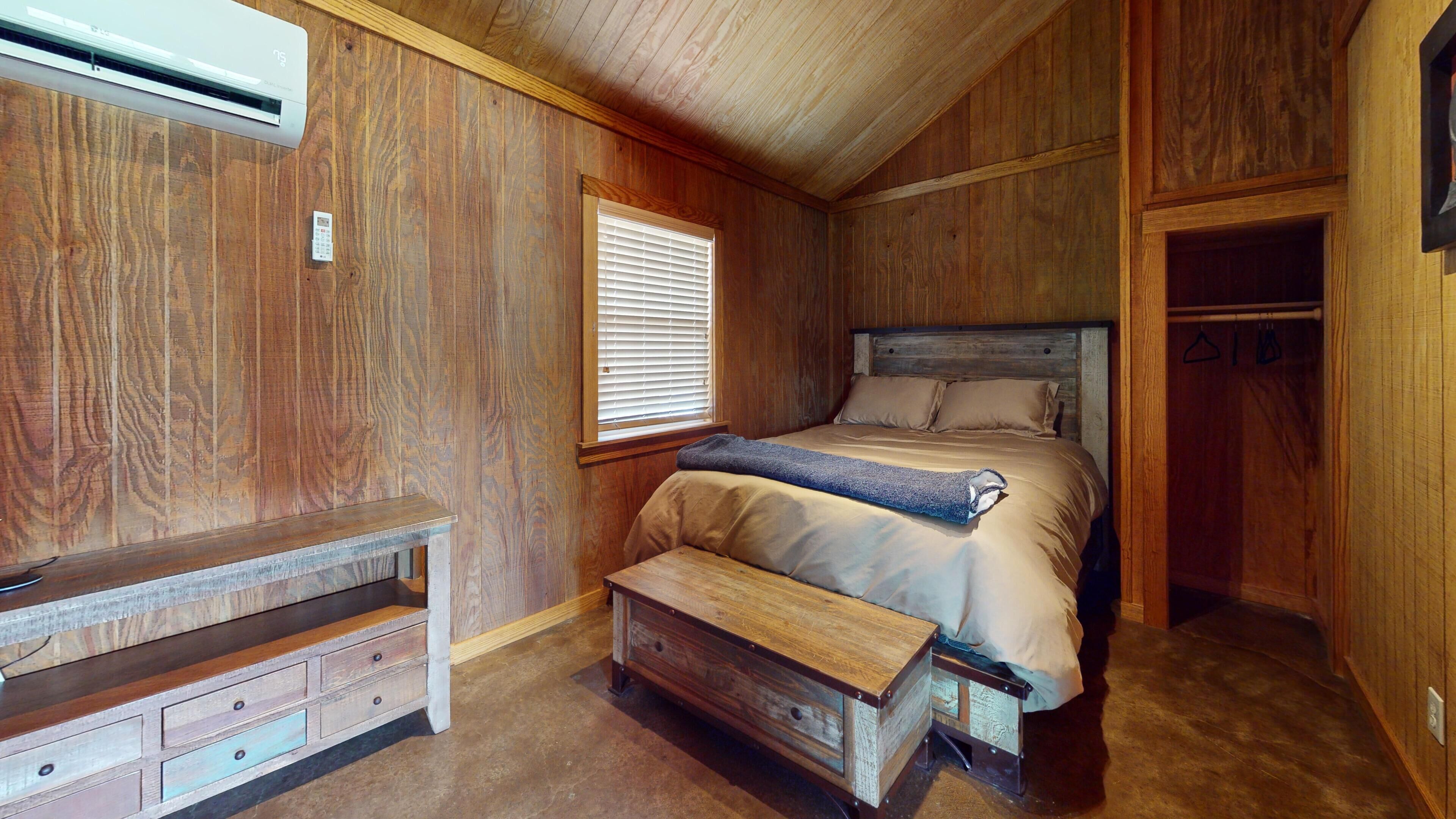 A bedroom with a wooden bed, a bench, a small table, and an air conditioning unit.
