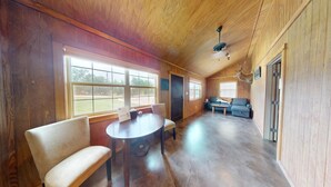 Une pièce spacieuse aux murs et au plafond en bois, avec une grande fenêtre, un canapé, une table et un ventilateur de plafond.