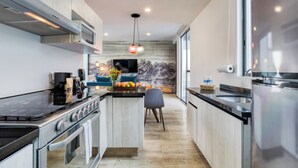 Una cocina moderna con electrodomésticos de acero inoxidable, una isla central y un comedor con un sofá azul y una televisión.