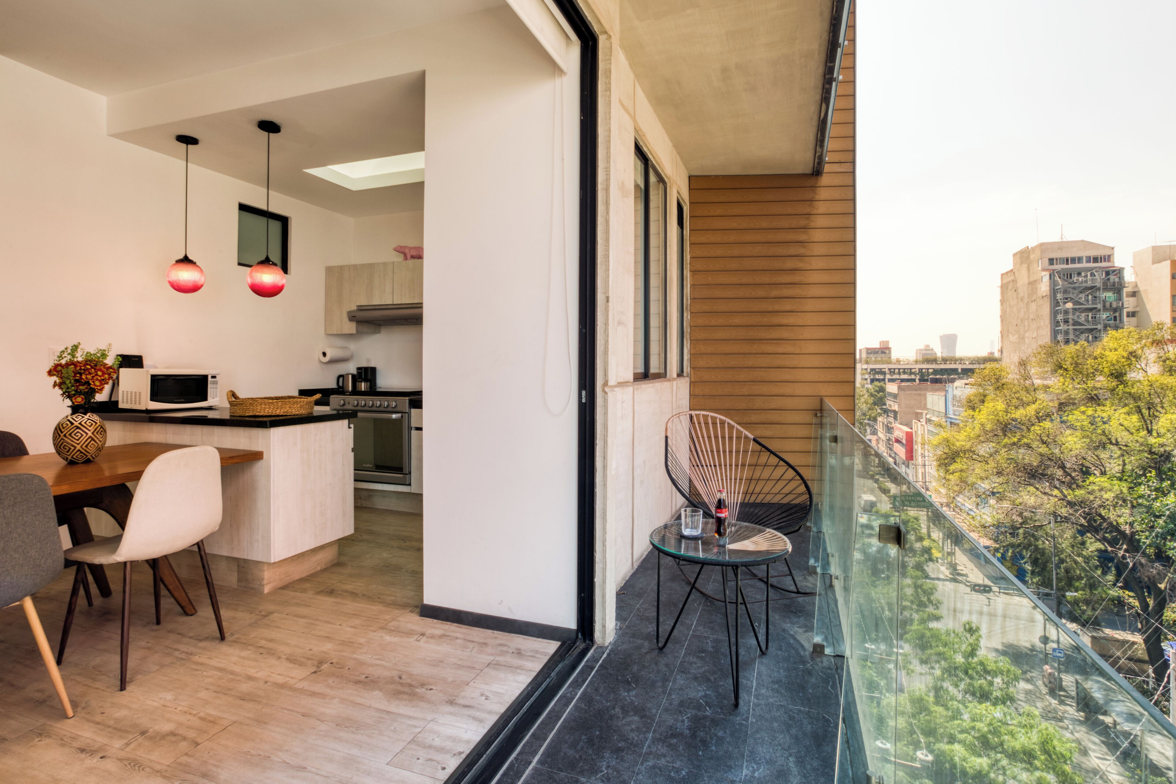 Een moderne keuken met een eetgedeelte, een balkon met glazen hekwerk en uitzicht op de stad.