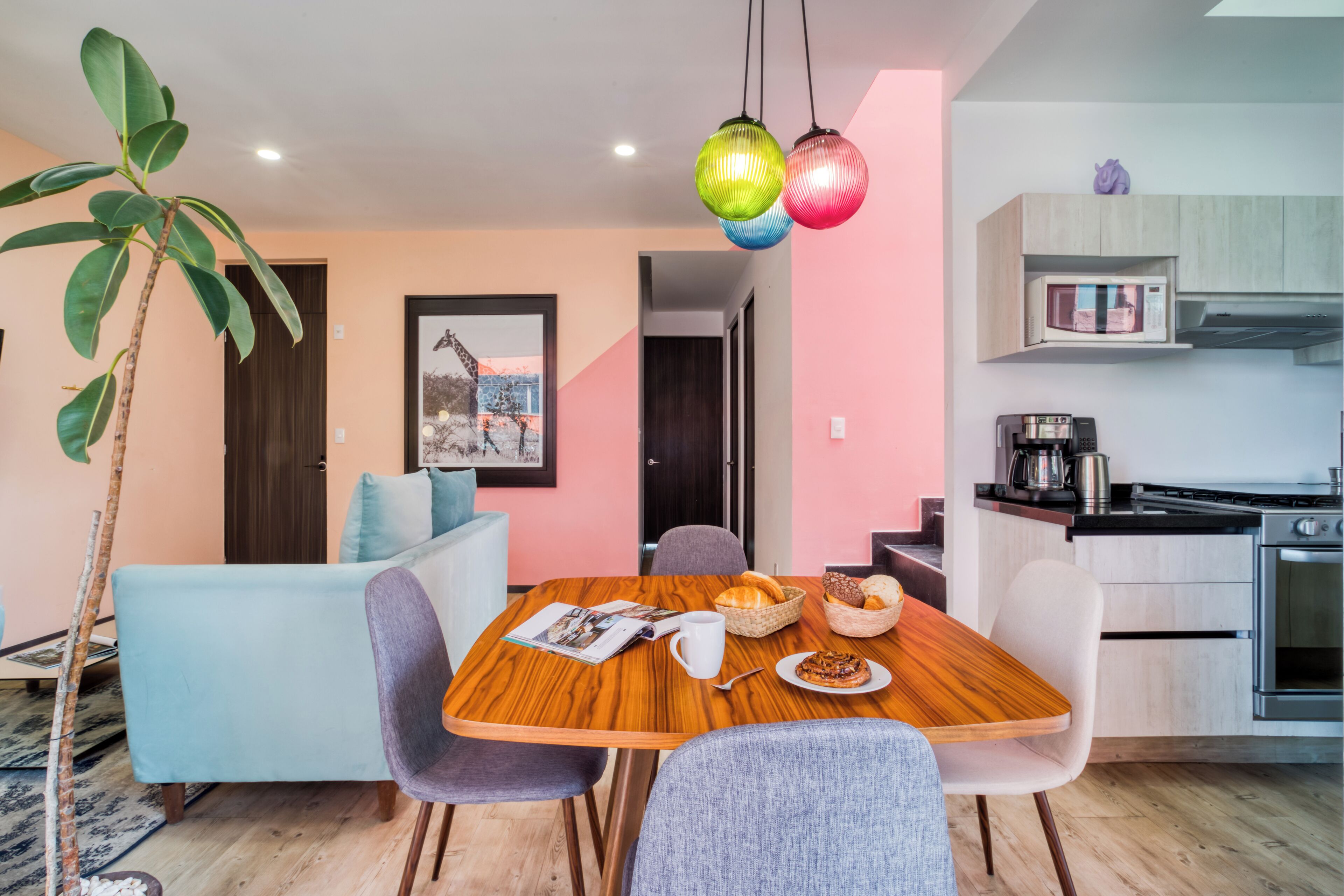 A modern kitchen with a microwave, stove, and cabinets. There is a dining table with chairs and a plant.