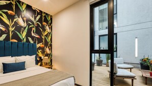 Una habitación de hotel moderna con una cama grande, cabecera azul y papel tapiz con motivos tropicales.
