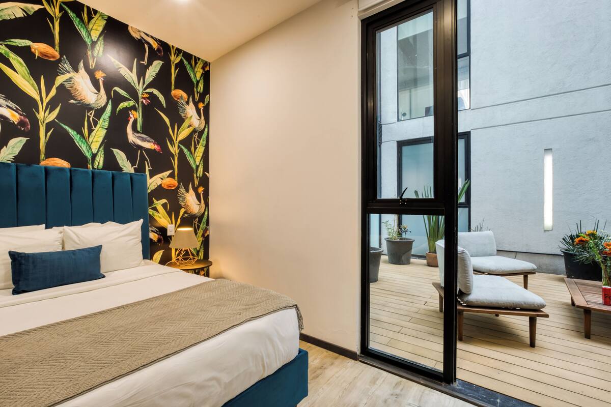Ein modernes Hotelzimmer mit einem großen Bett, einem blauen Kopfteil und tropischem Wandpapier.