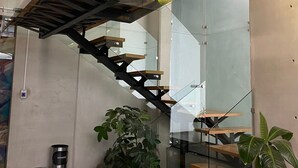 Un interior moderno con una escalera de cristal, bancos de madera y plantas en macetas.
