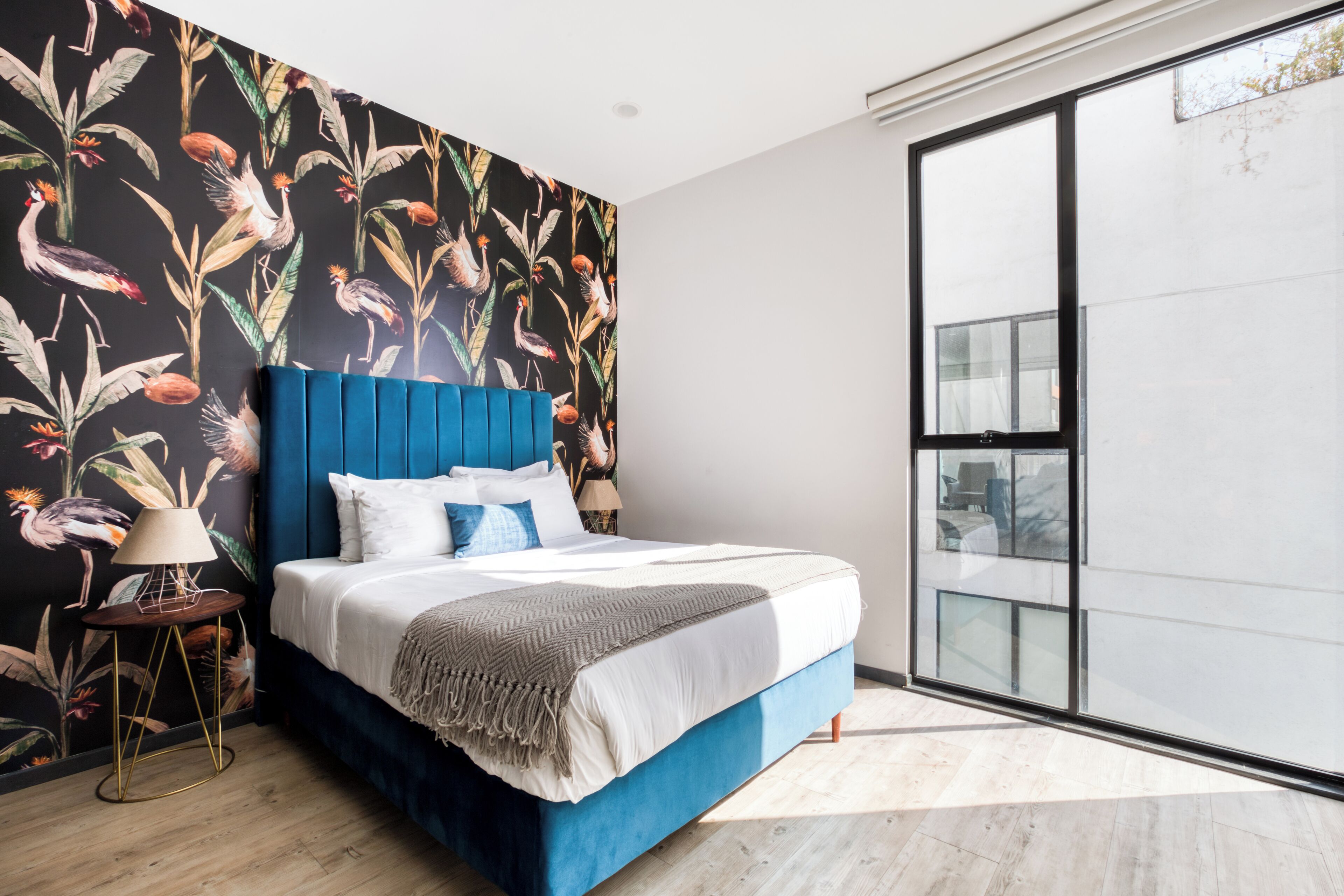 Ein modernes Schlafzimmer mit einem großen Bett, einem blauen Kopfteil und tropischem Wandpapier.