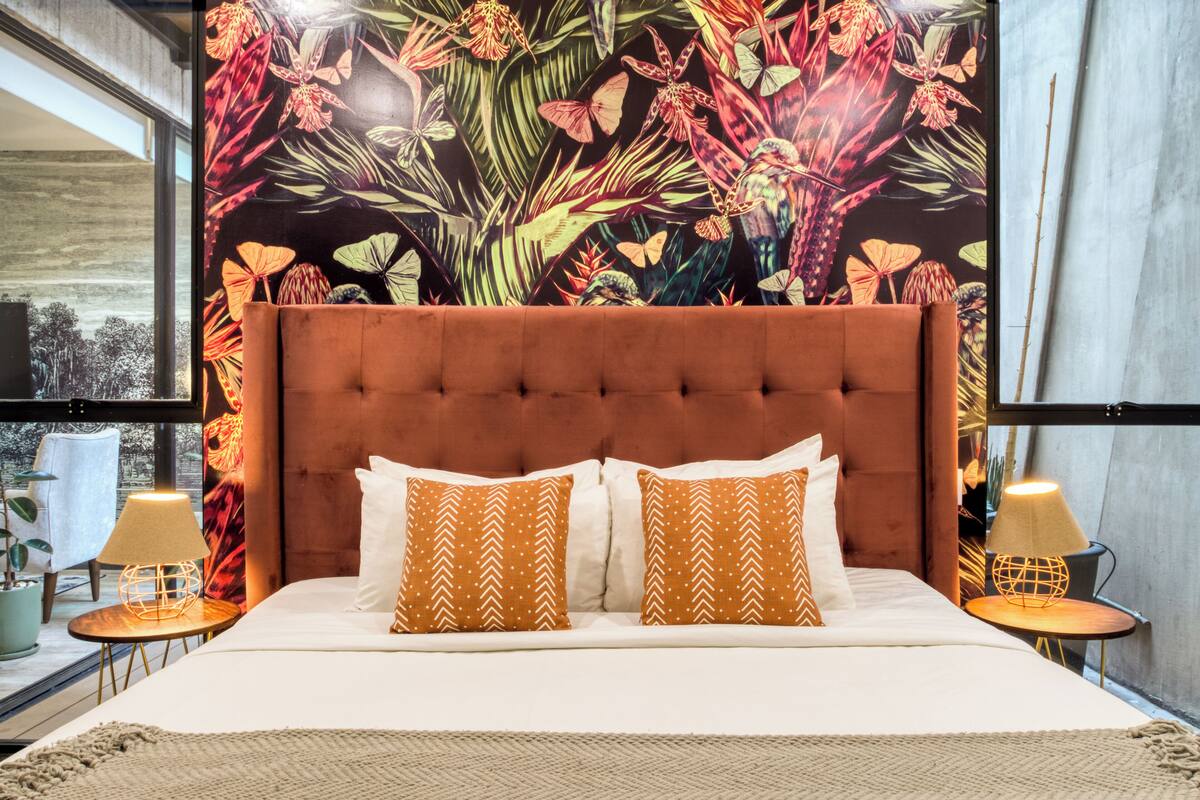 Ein Schlafzimmer mit einem großen Bett, zwei Nachttischen, einem Fenster mit Blick und einem floralen Wandteppich.