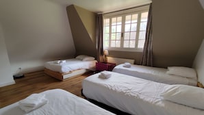 Un dormitorio con tres camas, suelo de madera, una ventana con cortinas y un radiador.