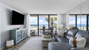 Un salon moderne doté d’un grand téléviseur, d’un canapé gris, d’une table basse et offrant une vue sur la plage grâce à de grandes fenêtres.