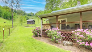A rustic cabin with a covered porch, surrounded by lush greenery and a wooden fence. - Cozy Mars Hill Farmhouse w/ Scenic Views (Mars Hill)