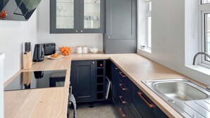 Une cuisine moderne avec des meubles de couleur sombre, un plan de travail en bois, un évier et une fenêtre.