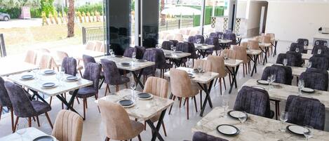 Un restaurant doté de nombreuses tables et chaises, disposées dans un espace intérieur vaste et lumineux grâce à de grandes fenêtres.
