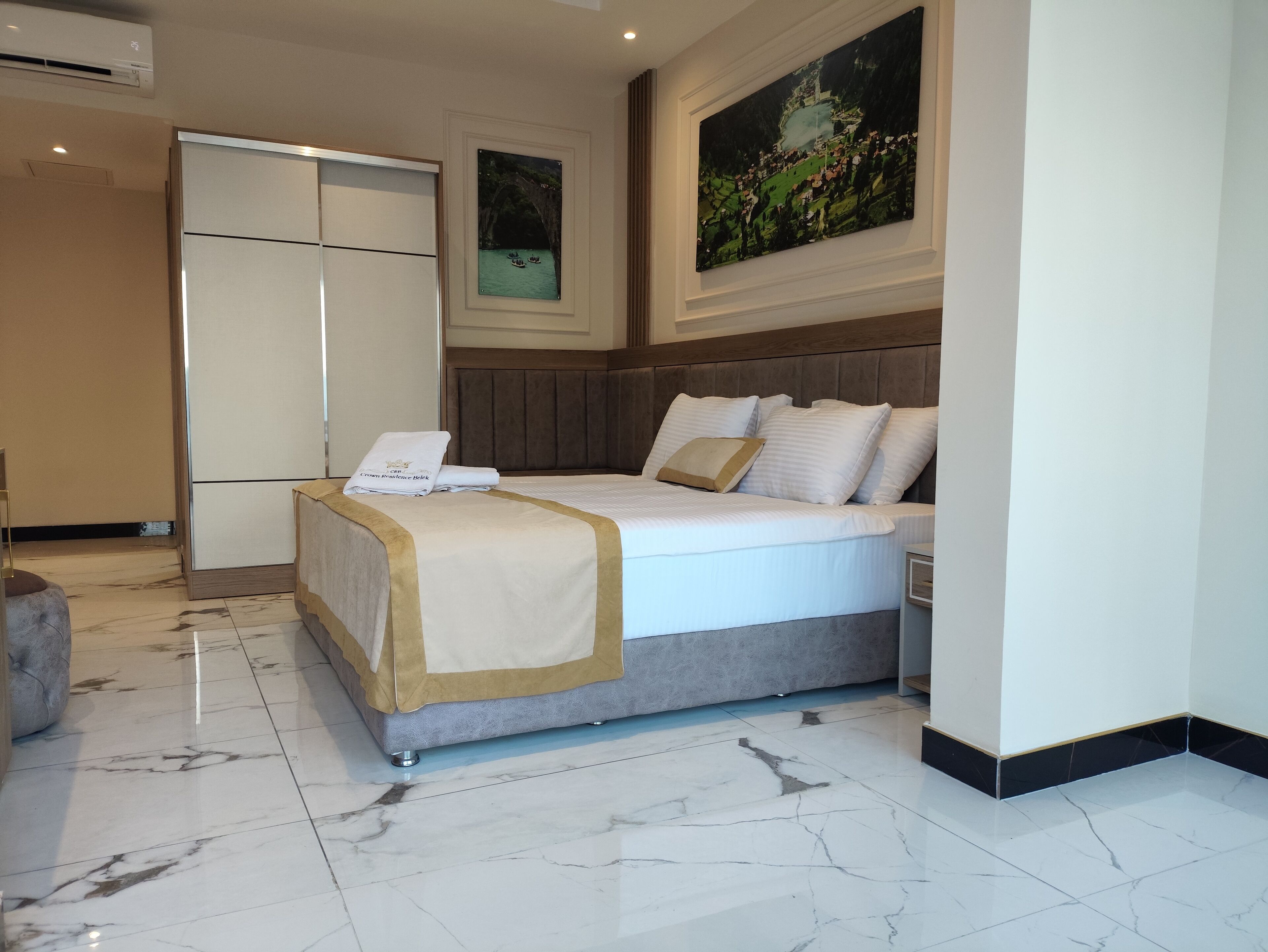 A hotel room with a bed, a desk, a chair, a wardrobe, and a painting on the wall.