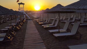 Ein Strand mit Reihen von Liegestühlen und Reetsonnen schirmen, einem Holzsteg und einem Rettungsturm.