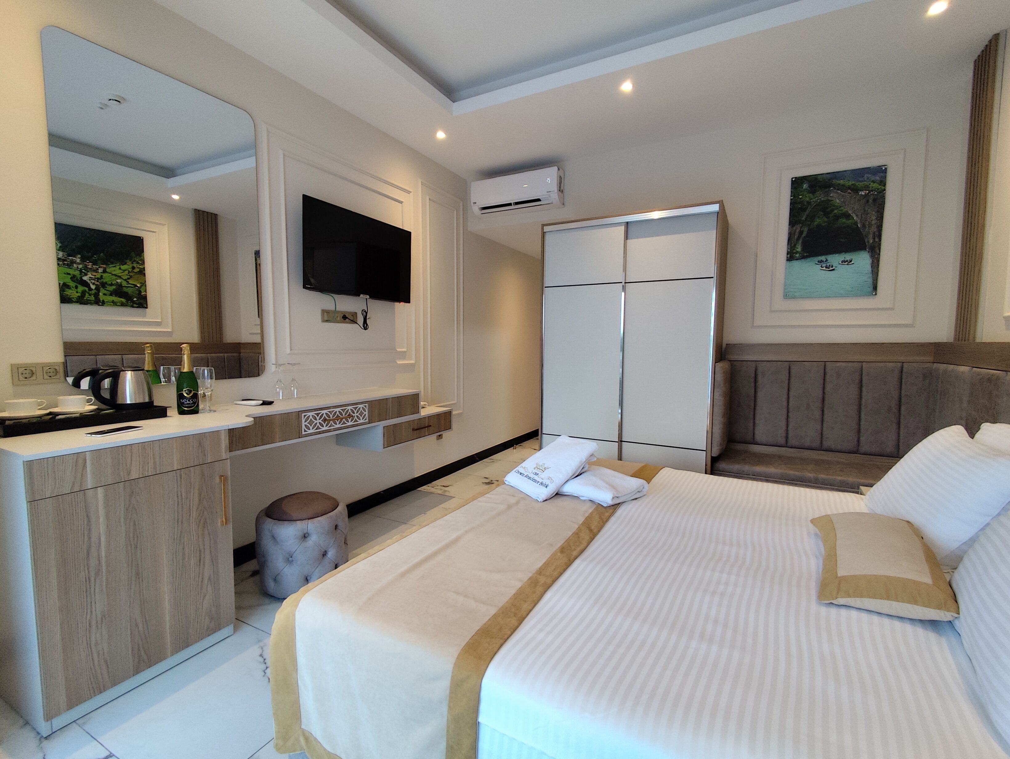 A hotel room with a bed, a vanity with a mirror, a television, a wardrobe, and a painting on the wall.