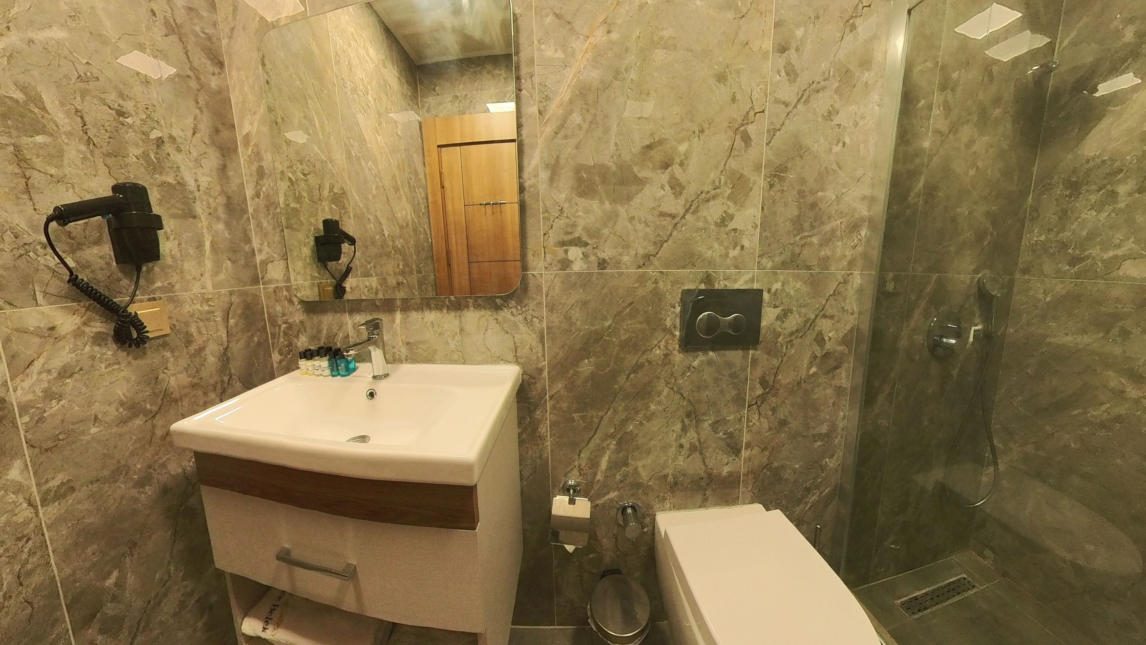 Un baño con lavamanos de mármol, un espejo, un armario de madera, una ducha y un inodoro.