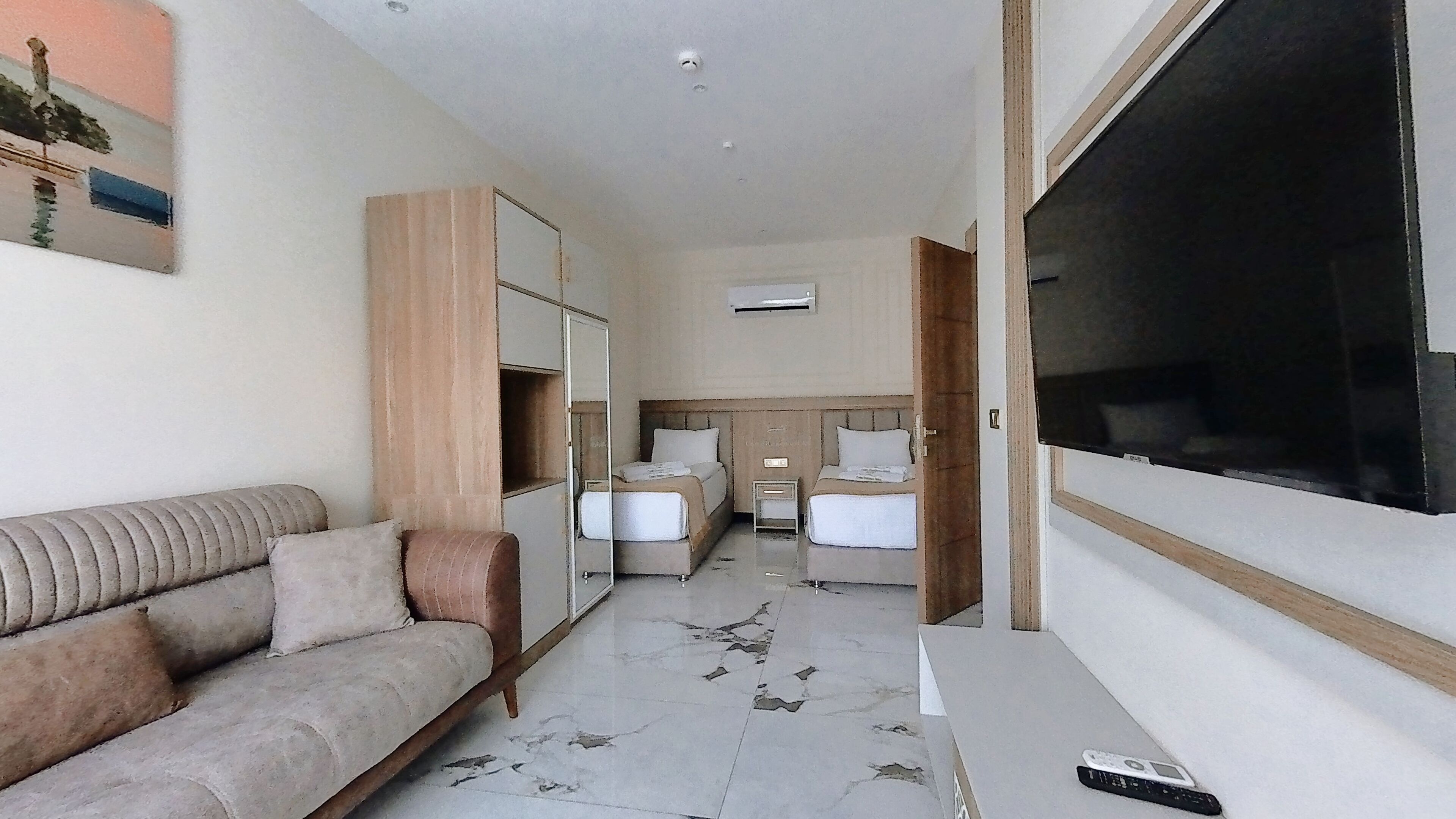 A hotel room with a sofa, two beds, a TV, and a painting on the wall.