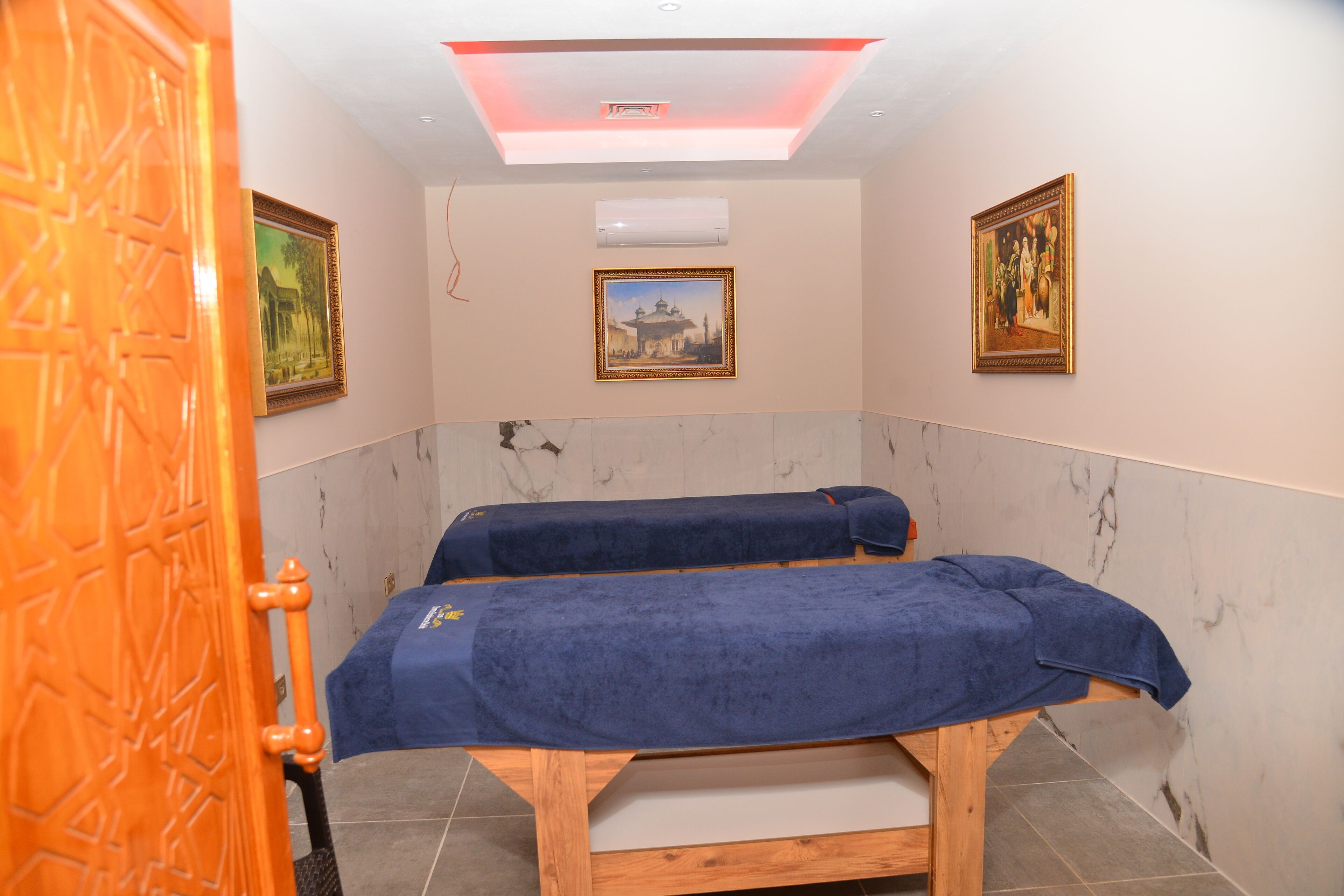 Ett rum med två massagebänkar, en taklampa och två inramade tavlor på väggarna.