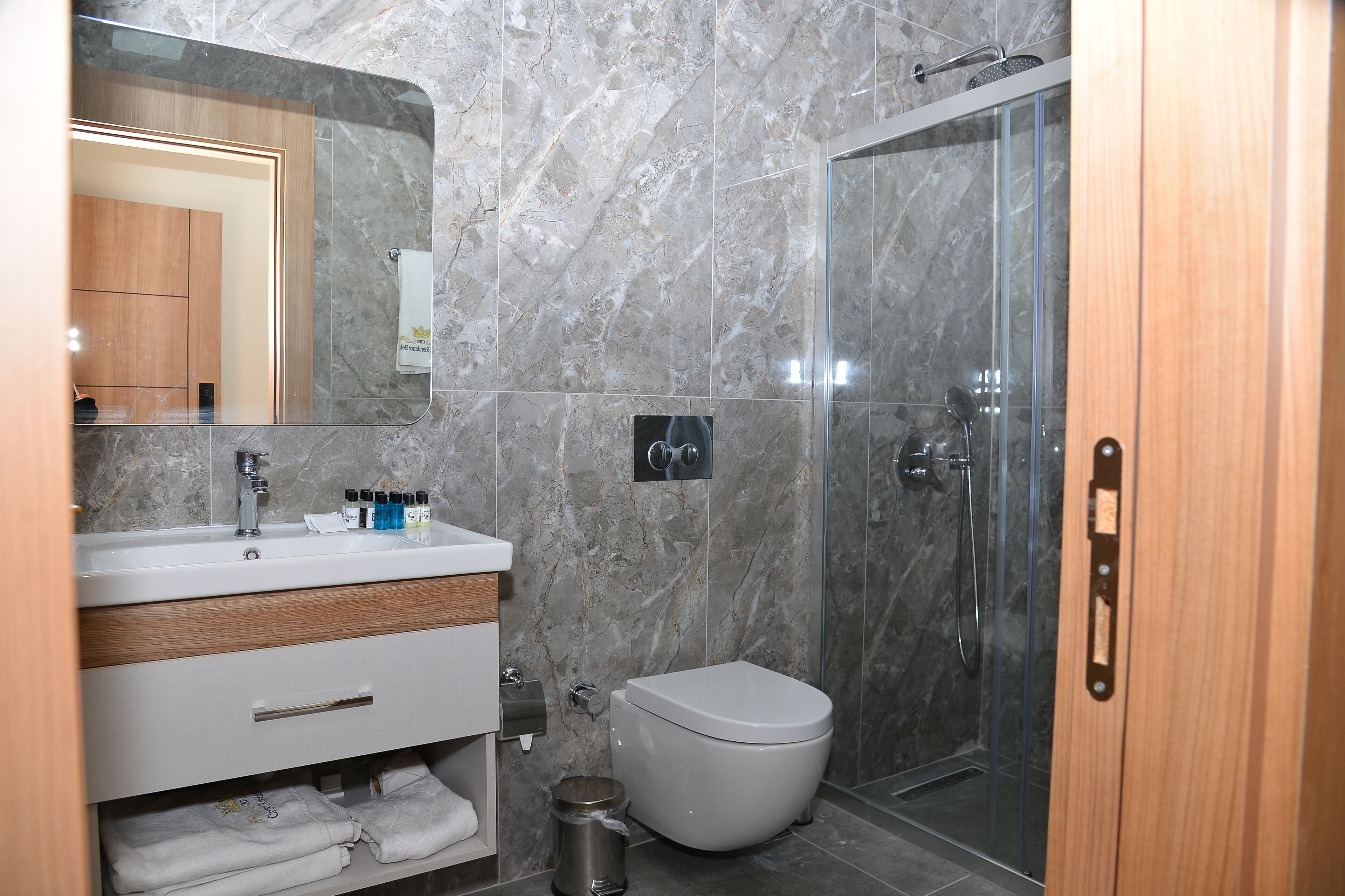 Un baño moderno con pared de mármol, un lavamanos blanco, un inodoro y una cabina de ducha de vidrio.