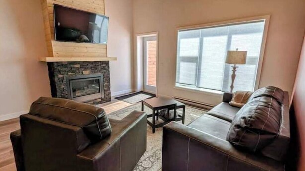 A living room with a stone fireplace, wooden ceiling, and large windows. - Yukon Hot Springs Villa #31 (Whitehorse)