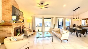 A spacious living room with a fireplace, comfortable seating, a dining area, and large windows. - Ajijic 2 Bedroom Unit-huge Patio-bikes-gym-pickleball Court-golf Cart-scooters (Chapala)