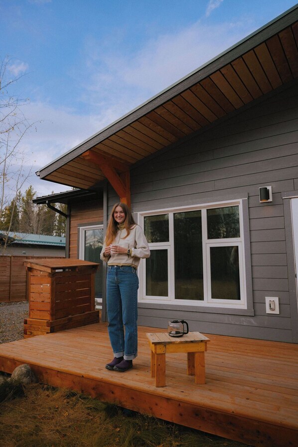 A person standing on a wooden deck in front of a house with large windows and a wooden exterior.