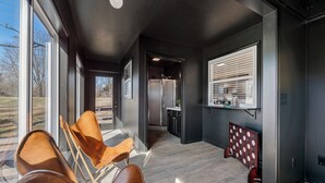 A modern interior with a kitchen area, a seating area with chairs, and a large window providing a view of the outdoors. - GameRoom, Trail access seconds away, cozy! (Bella Vista)