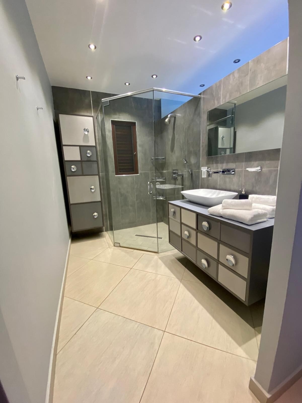 Een moderne badkamer met een glazen douchecabine, een ruim wastafelmeubel met een spiegel en een betegelde vloer.