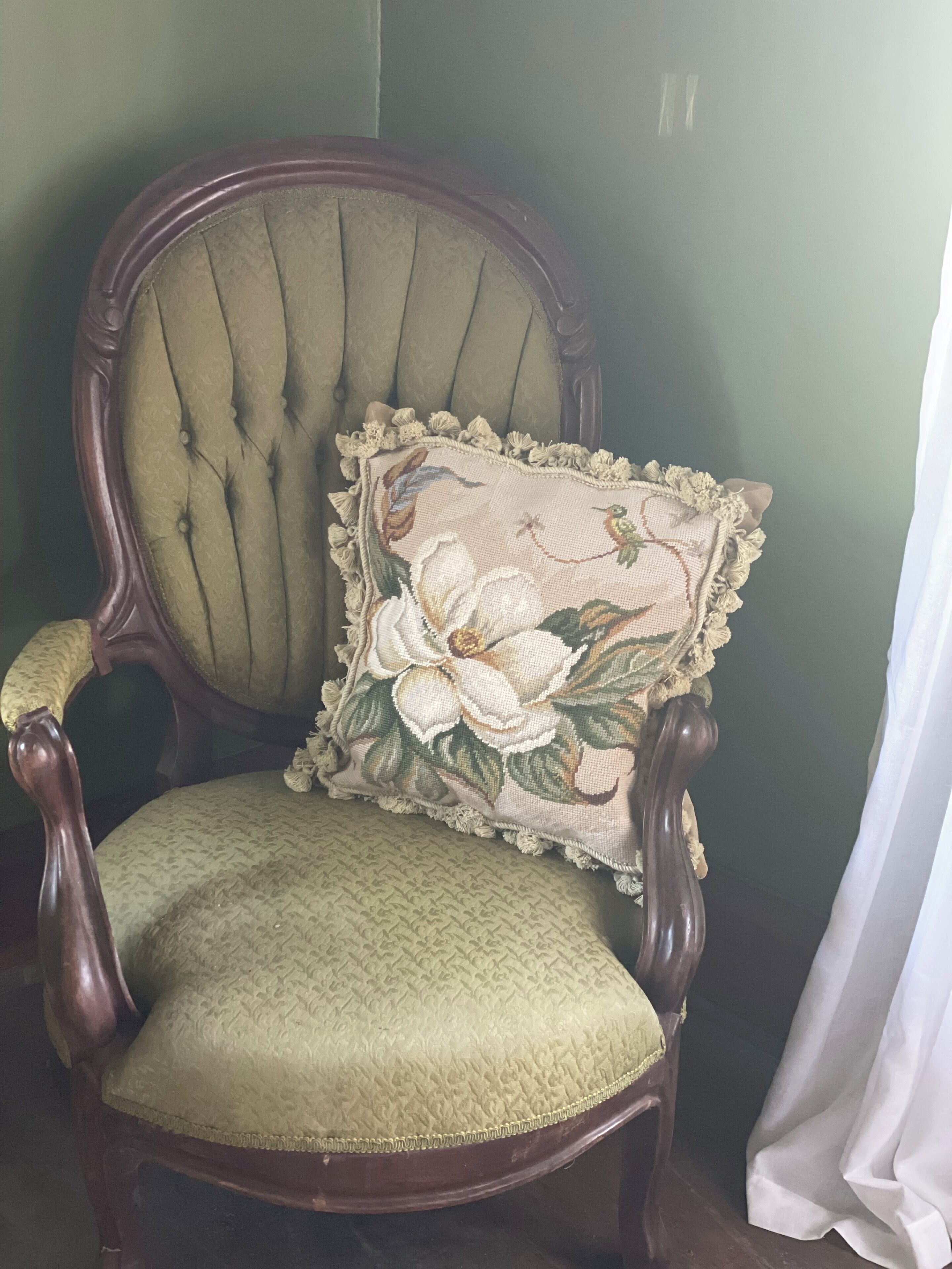 A green upholstered armchair with a decorative pillow featuring floral embroidery.