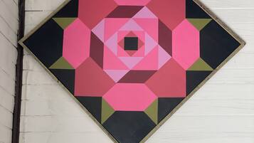 Obra de arte geométrica con forma de diamante, que presenta un hexágono central rodeado de formas concéntricas en rosa, negro y verde.