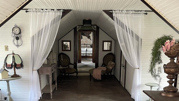 A cozy attic bedroom with a sloped ceiling, a bed with a canopy, and a rustic wooden floor. - Historic Carriage House Suite (Mannington)