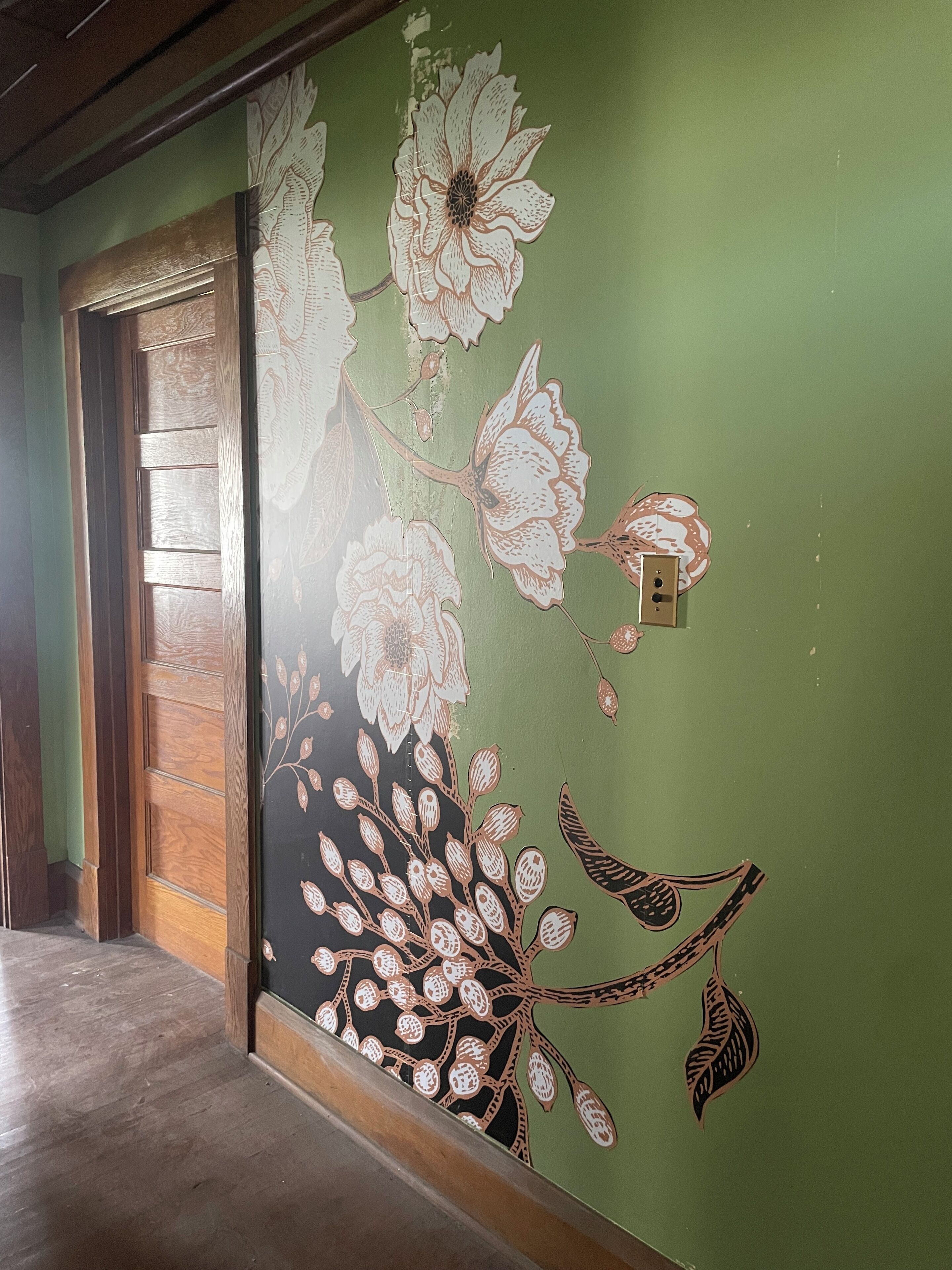 Pasillo con pared verde decorada con papel tapiz floral y una puerta de madera.