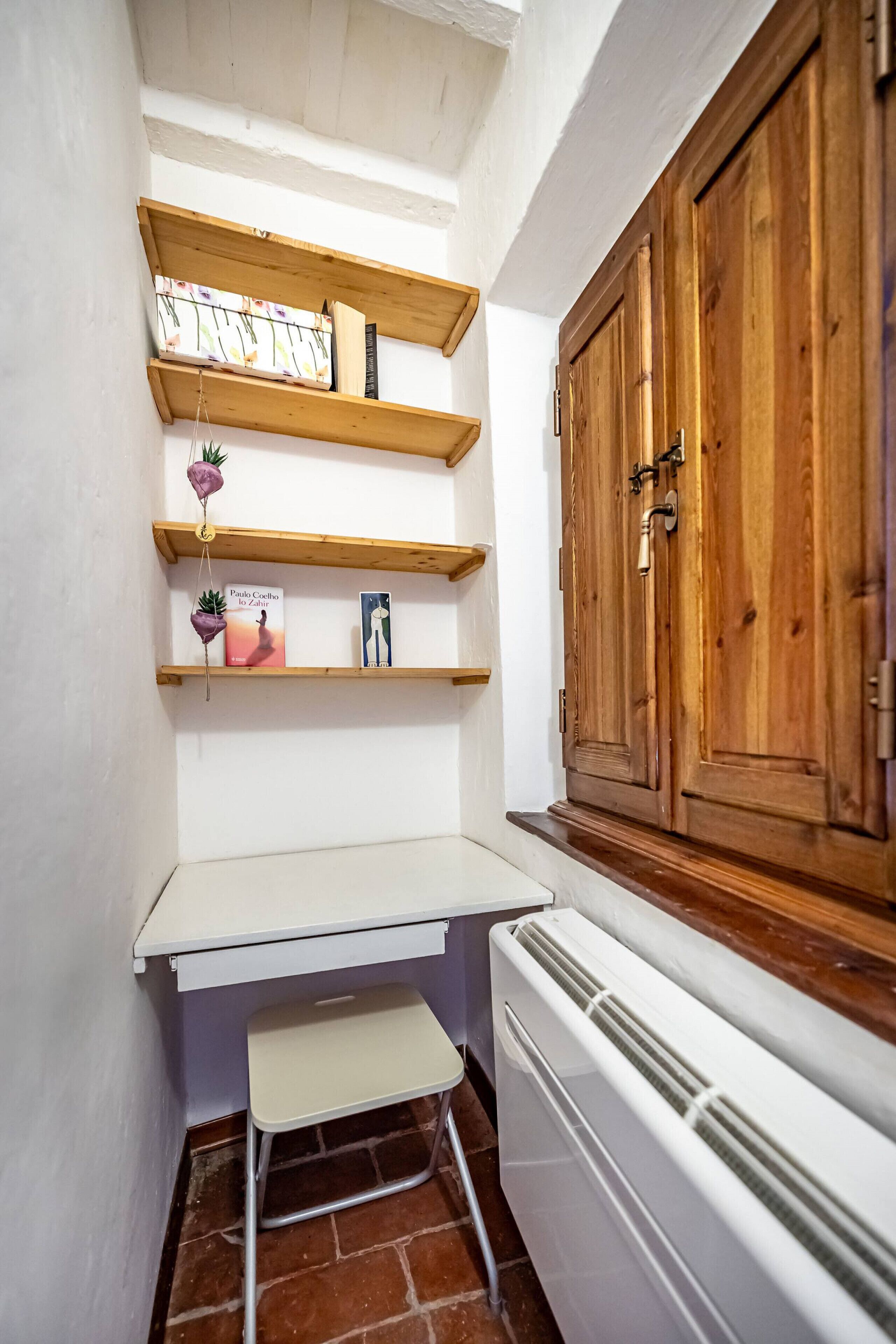 A small kitchen with wooden shelves, a white countertop, a radiator, and a wooden cabinet.
