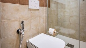 Baño con cabina de ducha de vidrio, inodoro y dispensador de toallas.