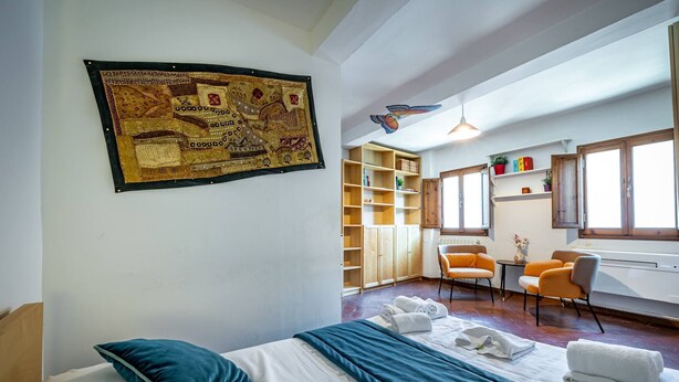 Habitación de hotel con cama, escritorio, silla, estantería y un gran tapiz en la pared.