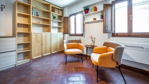 Una habitación con suelo de baldosas, estanterías de madera, dos sillones, un radiador y una ventana.