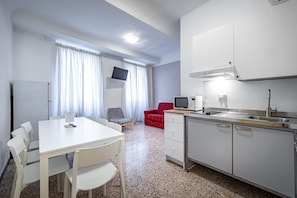 A compact kitchen with a white table and chairs, a red sofa, a TV, and a microwave.