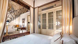 A bedroom with a large bed, a wooden nightstand, a desk with a chair, a staircase, and a wardrobe with glass doors. - YID Bargello luxury suite (Firenze)