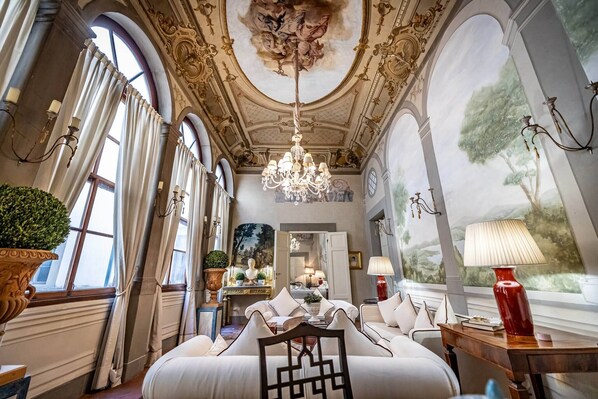 A luxurious room with a chandelier, large windows, and a mural on the wall.